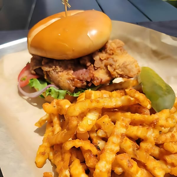 Crispy fried chicken sandwich with lettuce, tomato, and onion, served with crinkle-cut fries and a pickle.