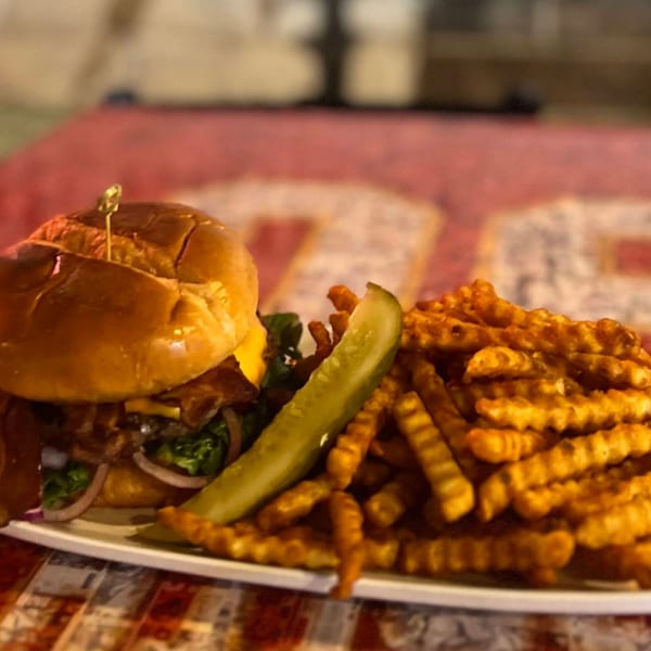 A juicy burger with cheese, bacon, lettuce, and onion, served with waffle fries and a pickle spear.