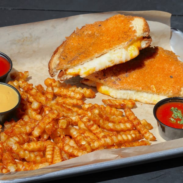 Grilled cheese sandwiches with melted cheese, waffle fries, and dipping sauces on a tray.