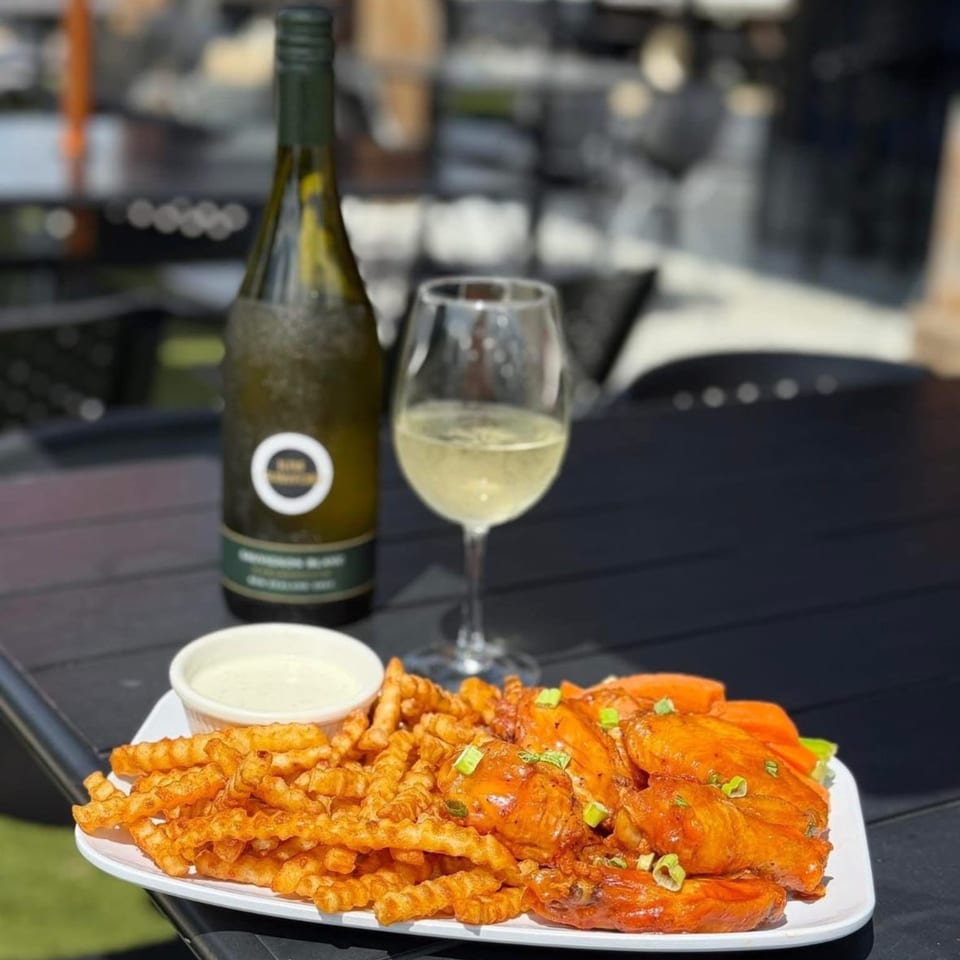 LOCAL's buffalo wings and crinkle fries with ranch, a glass of white wine, and a wine bottle.