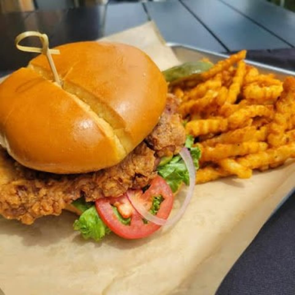 Crispy chicken sandwich with lettuce, tomato, onion, and crinkle-cut fries on a tray.