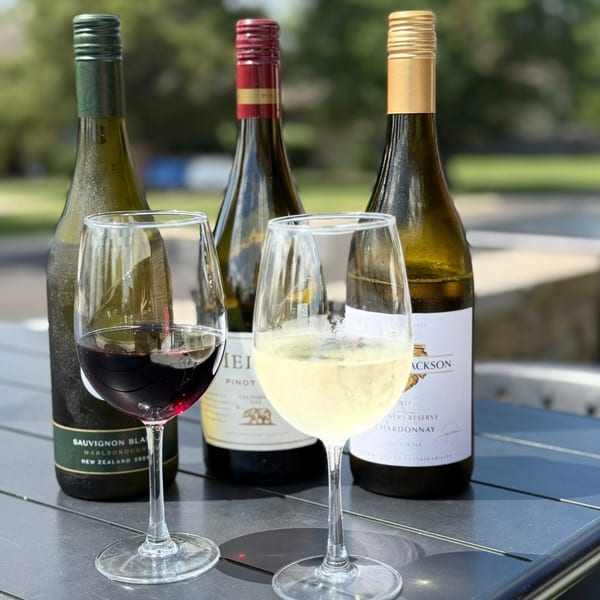 Three wine bottles and two glasses, one with red wine and one with white wine, on a table.