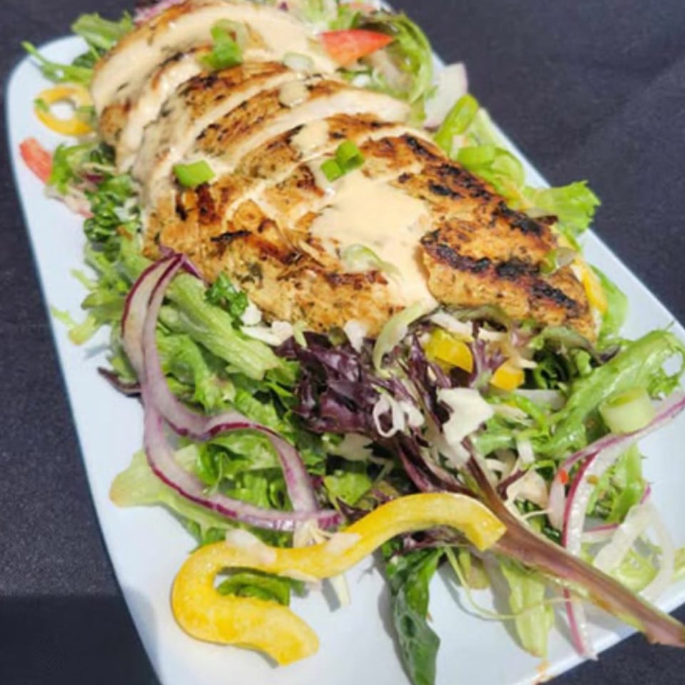Grilled chicken breast, sliced and drizzled with sauce, atop a fresh green salad with red onions and peppers.